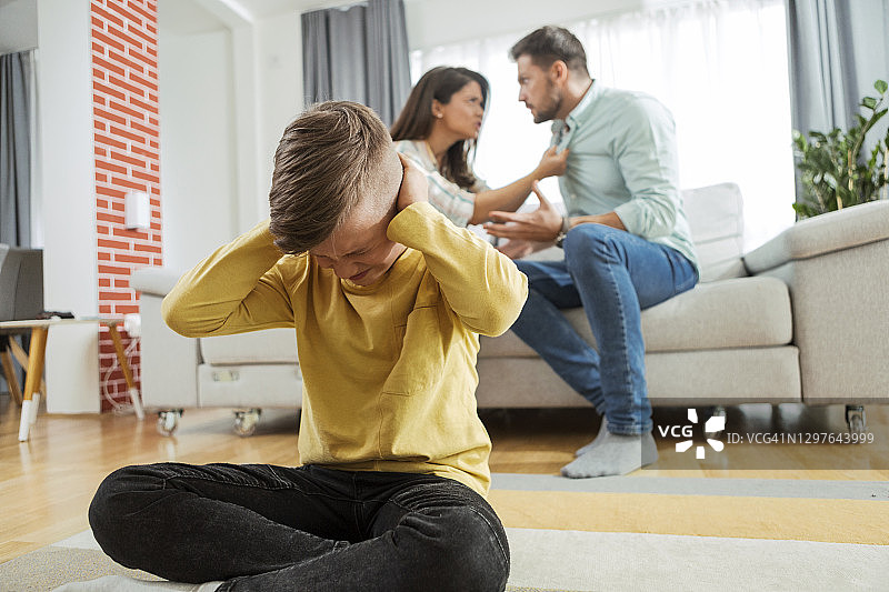 悲伤的男孩捂着耳朵听父母争吵图片素材