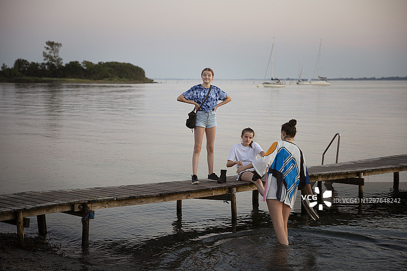 三个少女在夏季黄昏时分波罗的海沿岸码头上图片素材
