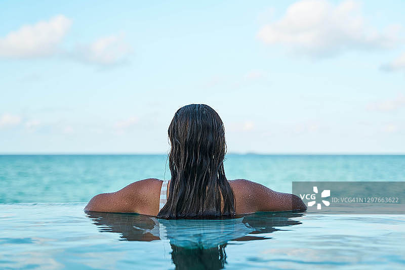 在游泳池里休闲并欣赏海洋的年轻女士（仅身体，面部不可见）图片素材