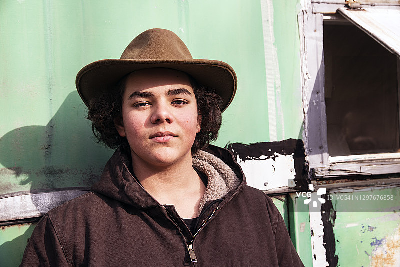 倚靠在饱经风雨的旧墙上的青少年男孩图片素材