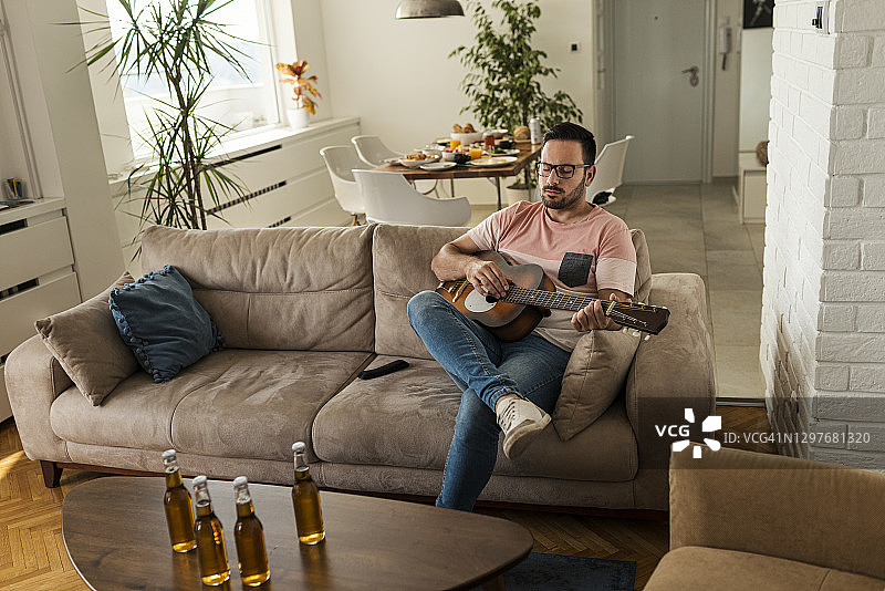 年轻男人在家弹吉他，等待朋友图片素材