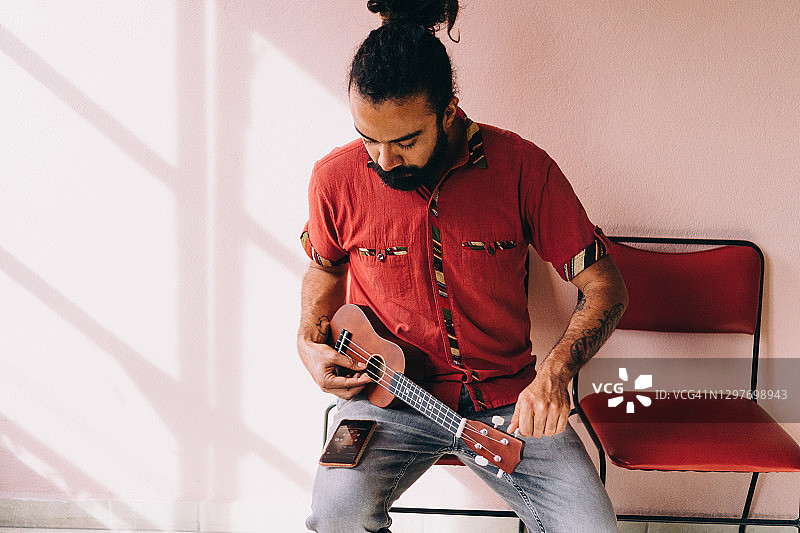 男子坐在椅子上用手机App调音尤克里里图片素材