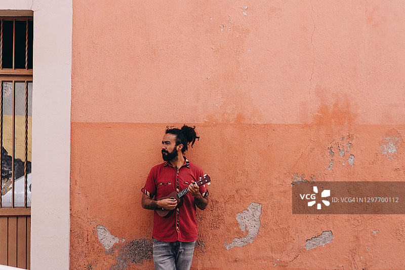 穿红衬衫的男人在橙色墙前演奏乐器图片素材