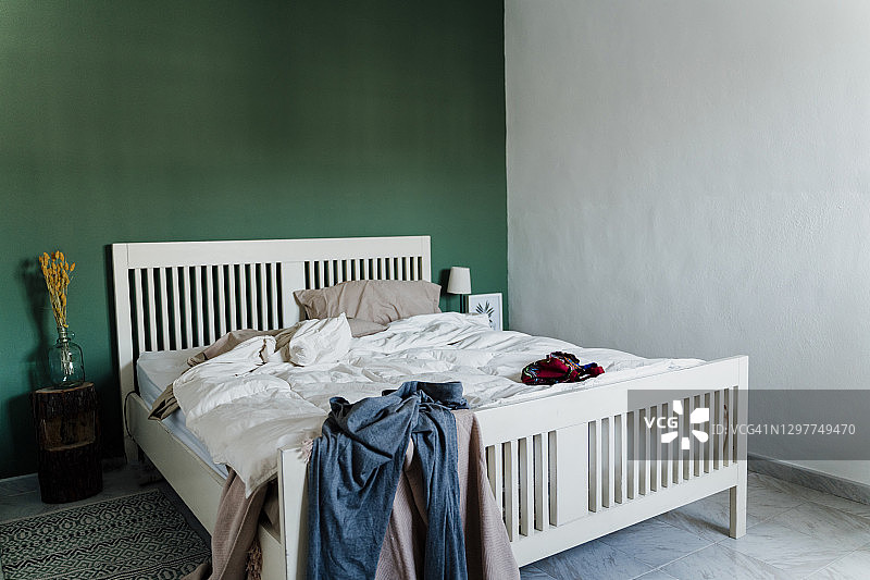 家里卧室里有羽绒被和衣服的凌乱床铺图片素材