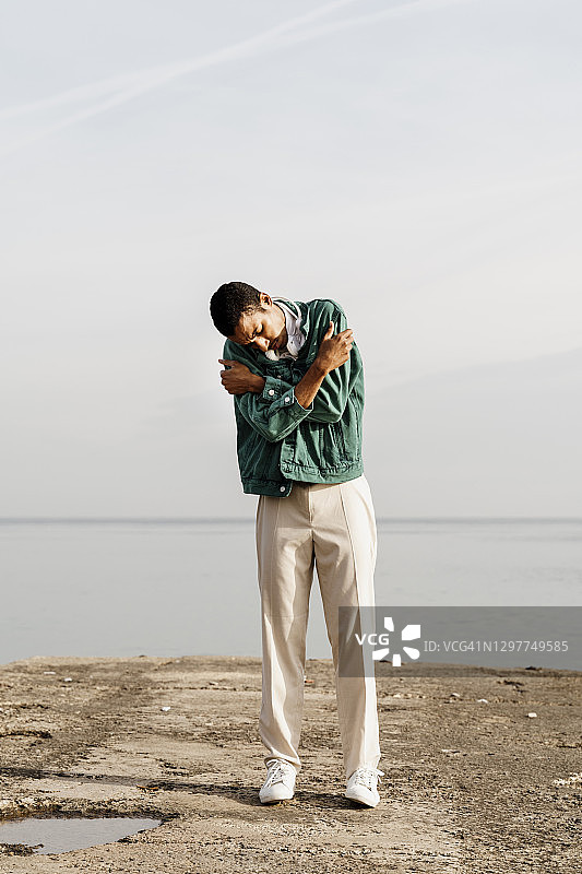 年轻男人拥抱自己，面对天空大海图片素材