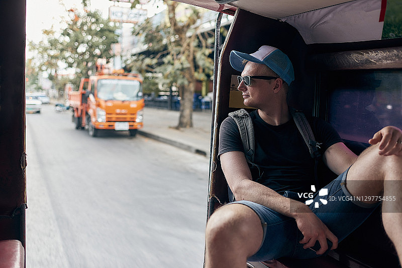 年轻男游客乘坐亚洲出租车欣赏城市风景图片素材