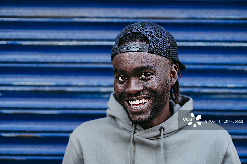 戴着帽子的快乐年轻人靠在蓝色瓦楞墙上图片素材