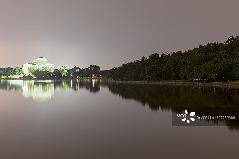 美国华盛顿特区，杰斐逊纪念堂和周围的树木在夜间映衬在潮汐湖中图片素材