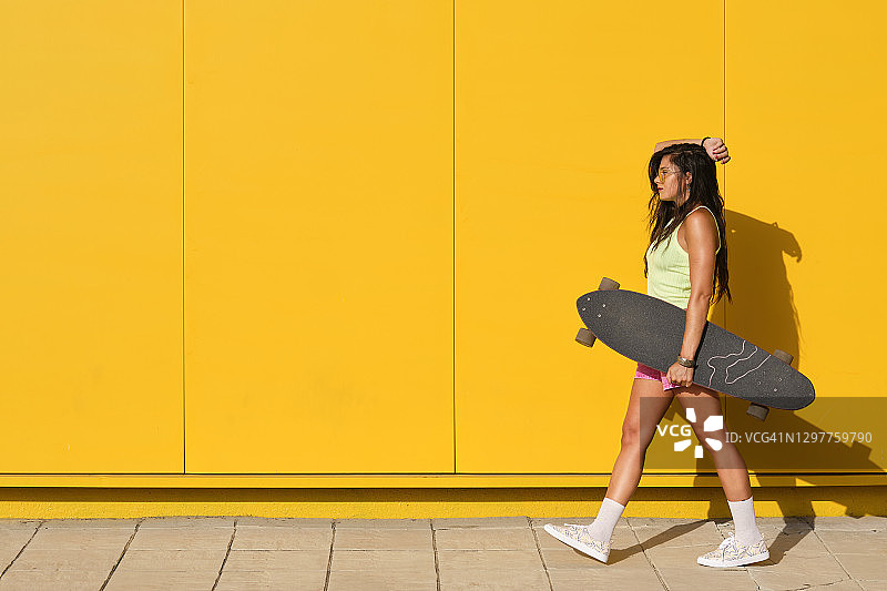 年轻女人手持长板走在黄色墙壁旁图片素材