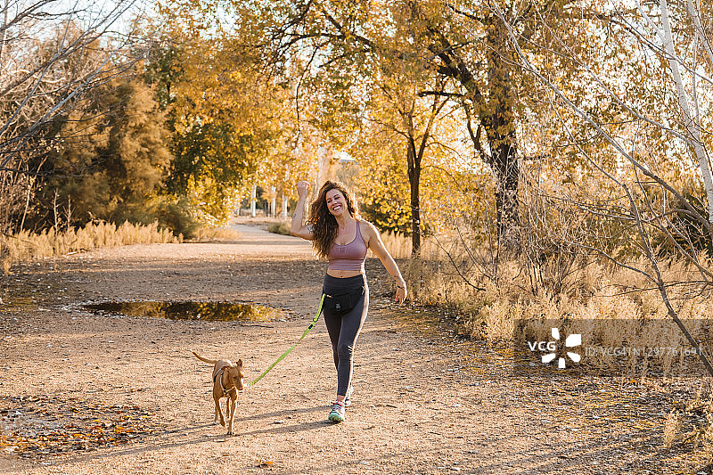 阳光明媚的日子里，笑容满面的女人带着她的狗在乡间散步图片素材