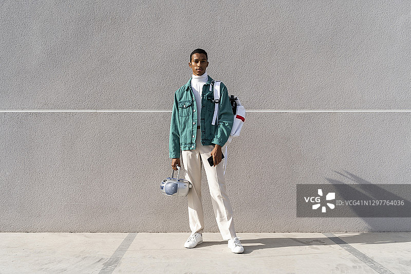 拿着收音机和包站在灰色墙前的年轻人图片素材