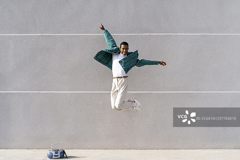 男人张开双臂对着灰色墙壁跳跃图片素材