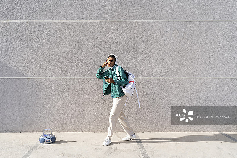 戴着耳机和手机，拎着包在人行道上跳舞的年轻男人图片素材