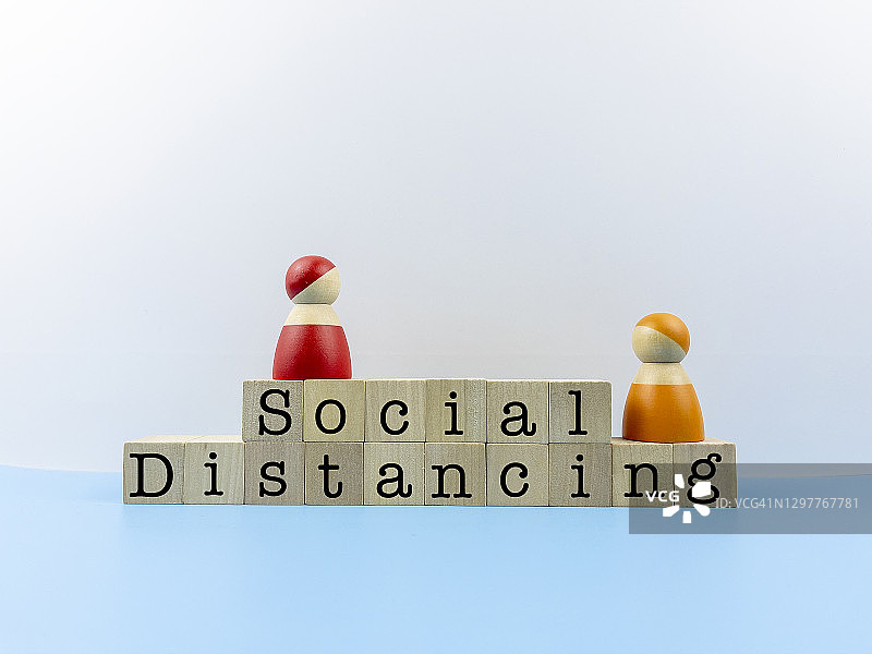 木块上的“社交距离”字样与两个女士木制复制品，健康、安全和新冠病毒概念图片素材