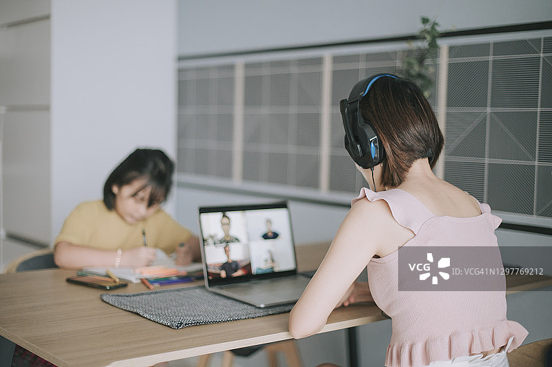 亚洲华裔母亲在家工作视频通话女儿在旁画画图片素材