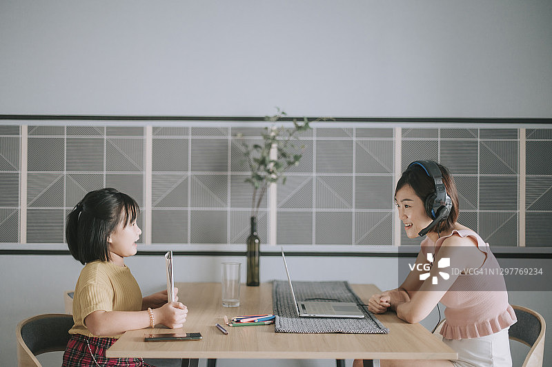 亚洲华裔母亲在家工作视频通话女儿在旁画画图片素材