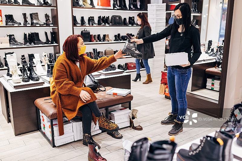 鞋店里的专业女售货员递给顾客合适尺码的靴子，以便试穿图片素材