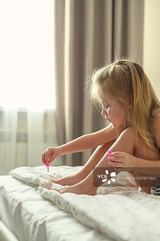 金发小女孩在家里沙发上用亮粉色指甲油涂抹脚趾甲图片素材