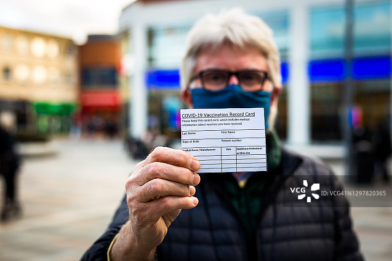 拿着新冠疫苗接种记录卡的年长男人图片素材