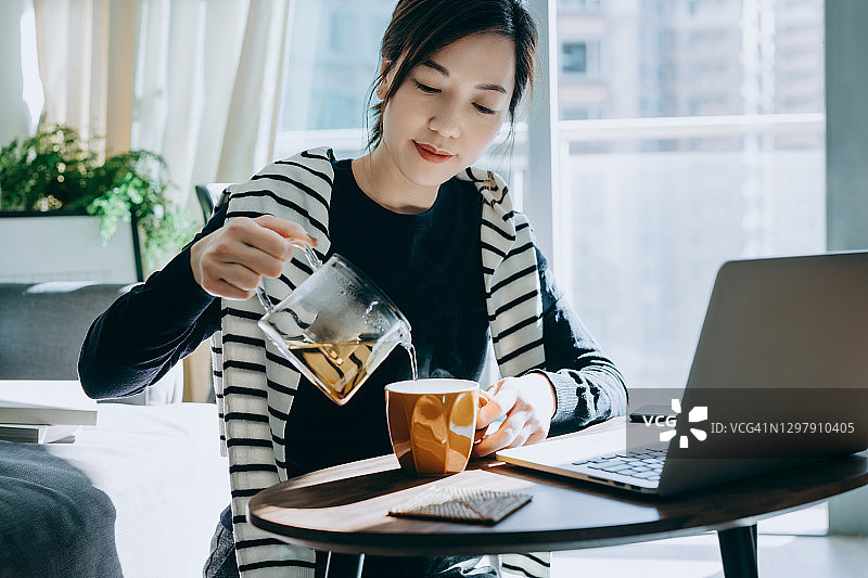 年轻的亚洲女人将茶从透明茶壶倒入杯中：健康生活方式图片素材