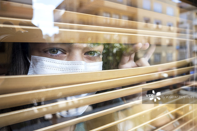 戴着口罩在家望向窗外的少女图片素材