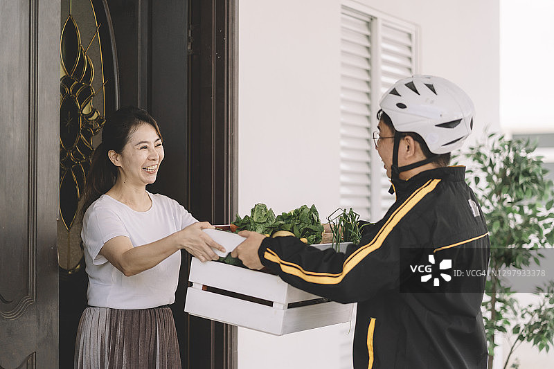 亚洲中国女人在家接收送货员外卖订单图片素材