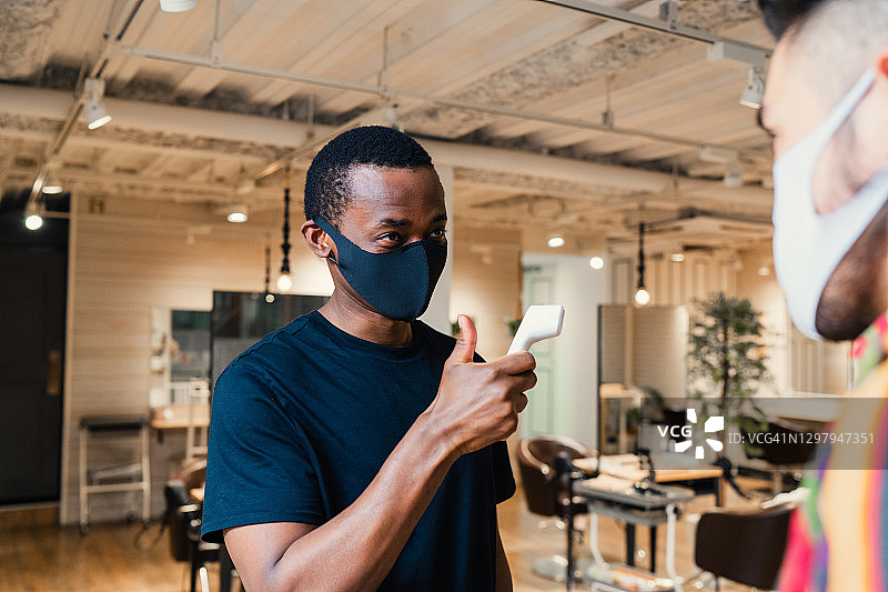 理发店老板用红外线温度计检查顾客的体温图片素材