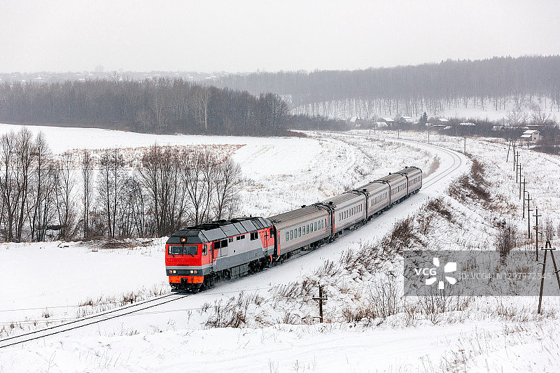 现代柴油机车牵引客运列车穿过白雪皑皑的乡村图片素材