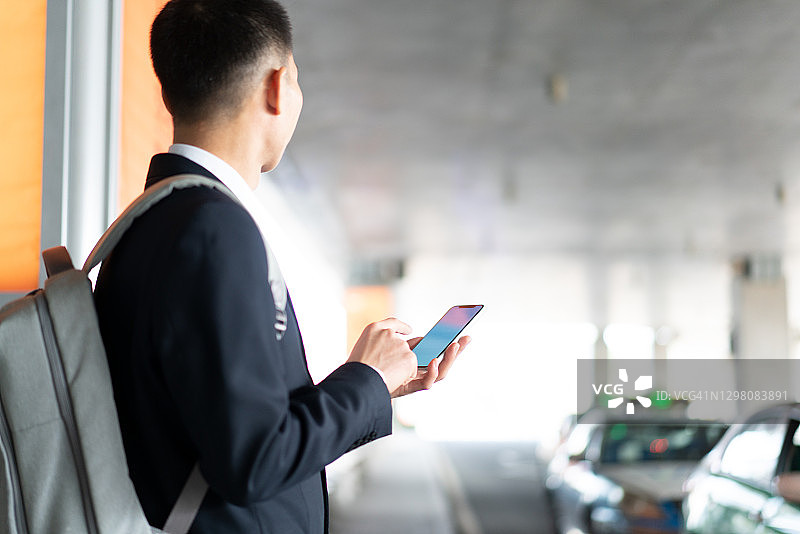 在路边等公共汽车，拿着手机的亚洲男人图片素材