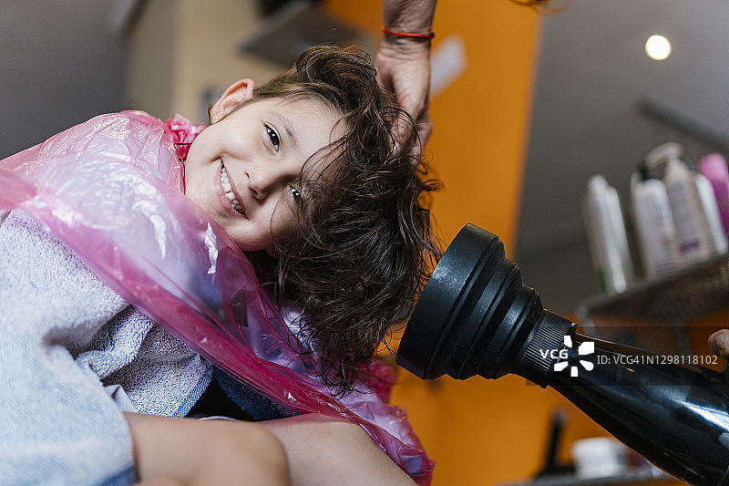理发师用吹风机为顾客吹干头发，女孩在沙龙里享受图片素材