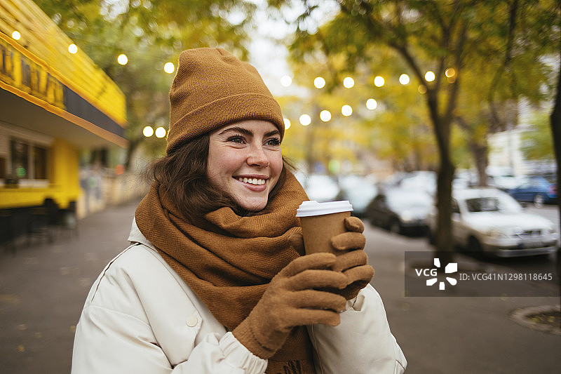 冬天在街上戴着针织帽，拿着一次性咖啡杯做白日梦的快乐女人图片素材