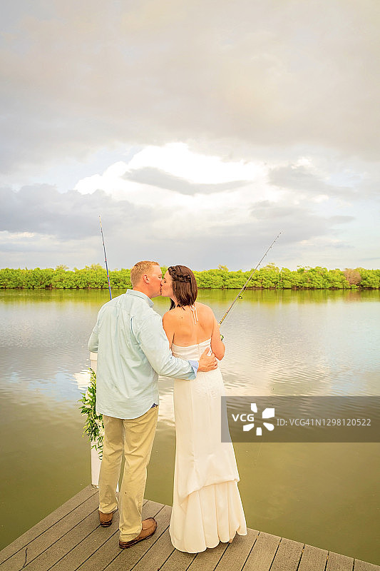 新娘新郎在海湾旁手持鱼竿亲吻图片素材