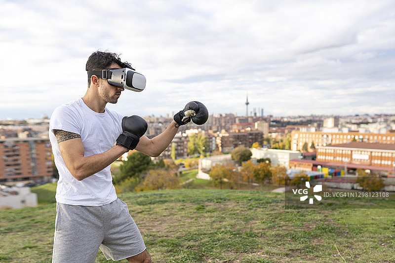 男性杂技演员戴VR头显在城市山丘上练习拳击图片素材