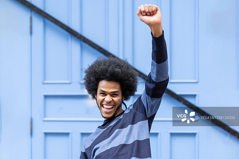 靠在蓝色墙壁上，举起手臂尖叫的快乐年轻男人图片素材