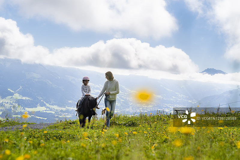 母亲在阿尔卑斯草甸上和小女儿一起骑小马图片素材