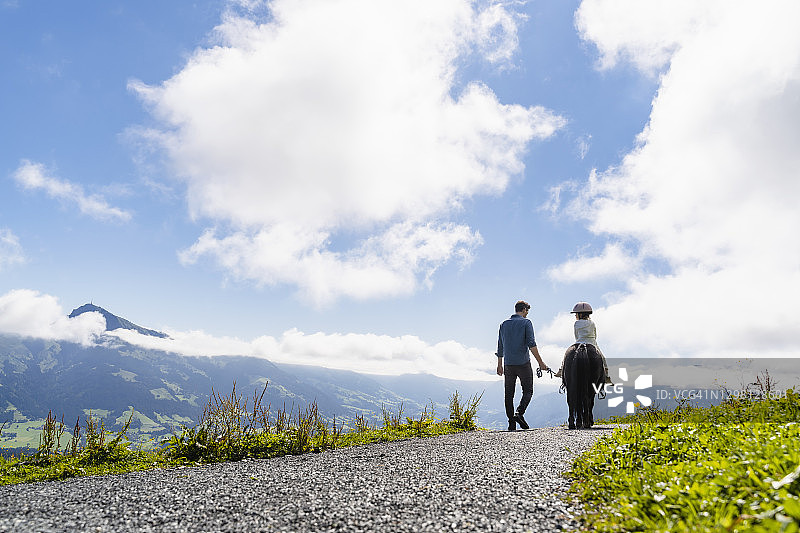 父亲沿着高山小路走在骑小马的女儿旁边图片素材