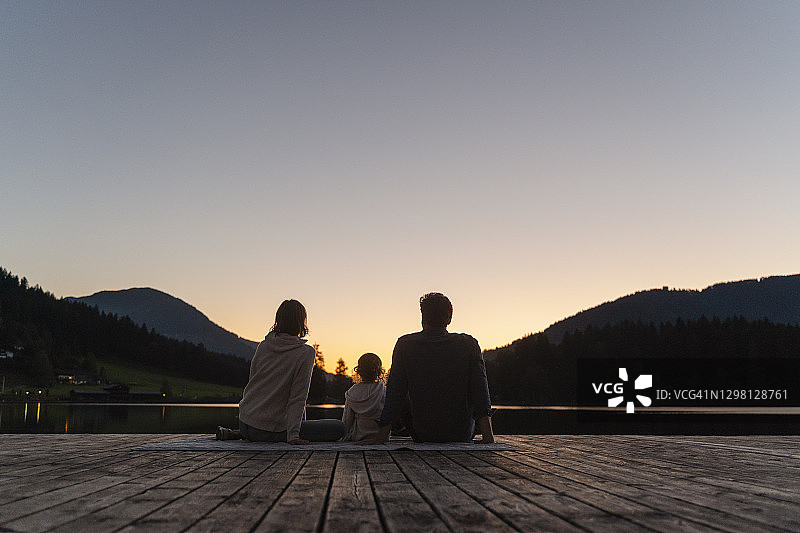 黄昏时分，与小女儿一起坐在湖岸码头尽头的家庭图片素材
