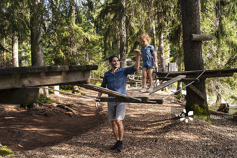 父亲帮助女儿走过森林障碍训练场上的小吊桥图片素材