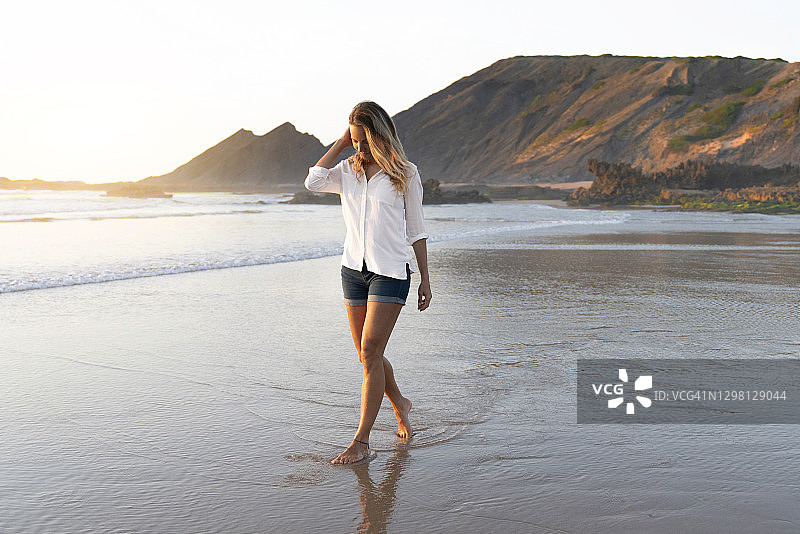 中年妇女在海滩上行走，低头看着水面图片素材