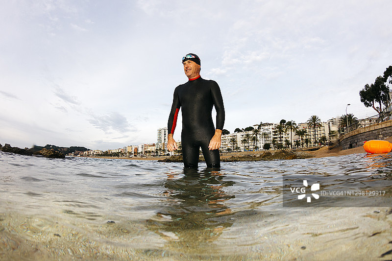 西班牙赫罗纳省滨海略雷特，男子站在及膝深的海水中，背景是城镇图片素材