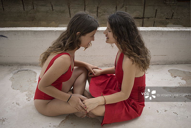 姐妹穿着红色衣服，在露台上对面而坐图片素材