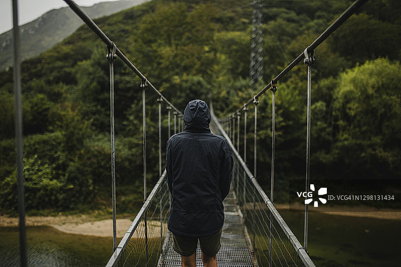 穿着雨衣站在森林中塞拉河悬索桥上的女人图片素材