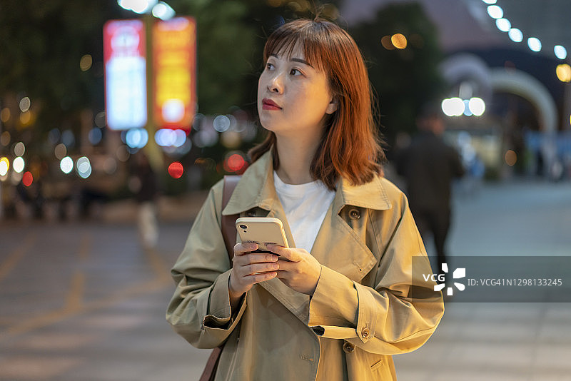 夜晚街头看手机的亚洲年轻女人图片素材