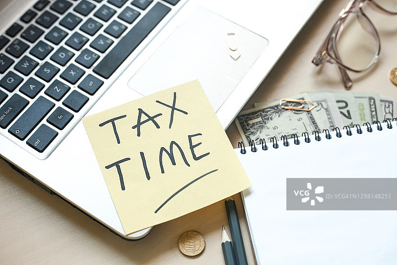 木桌上的记事本、铅笔、笔记本电脑、眼镜、钱和办公用品，税务时间或税务日概念图片素材