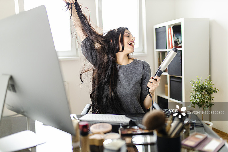 疫情期间，女子在梳妆台前看电脑，边上网课边用卷发棒图片素材