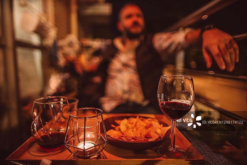 在阳台上，在烛光下与朋友们一起享用小吃和葡萄酒的白人男子图片素材
