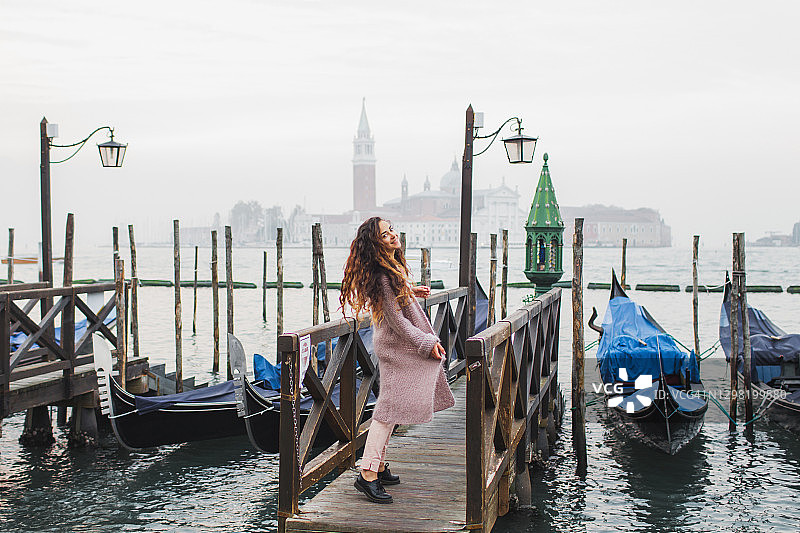 游客女性在威尼斯泻湖边漫步，背景是传统贡多拉图片素材