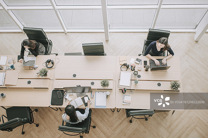 俯视：佩戴防护口罩的亚洲中国女性在开放式办公室工作，遵守新的SOP和社会疏远，预防疾病图片素材