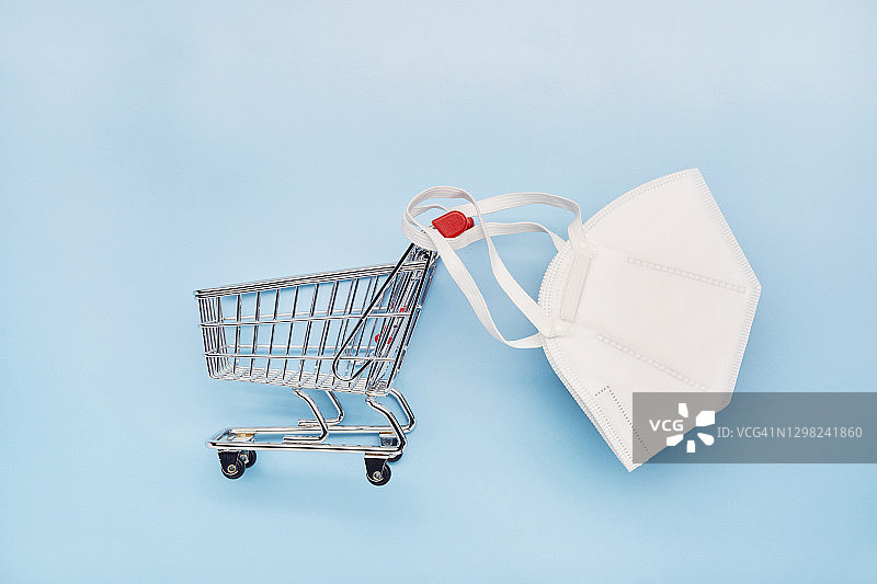 蓝色背景上的白色FFP2防护口罩和小购物车静物图片素材