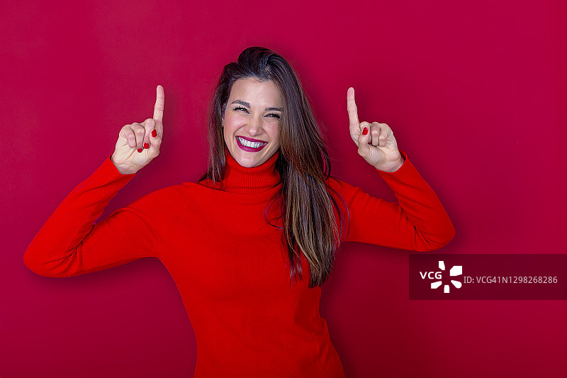 穿红色高领毛衣的长发女人面带微笑举起食指，幸福概念图片素材